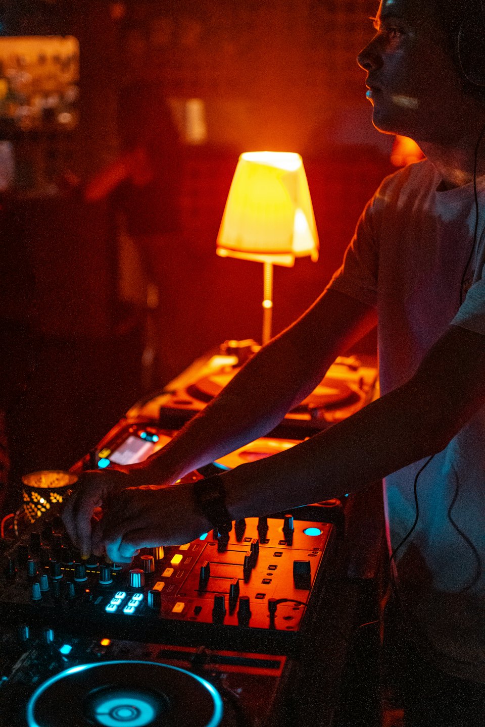 Manos de DJ sobre un controlador iluminado en un club oscuro.