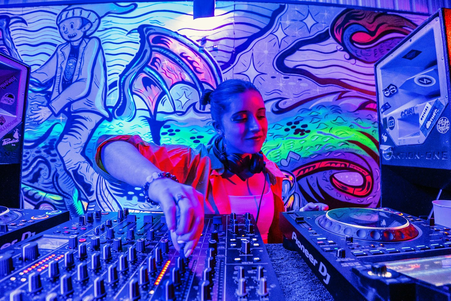Mujer con camisa naranja ajusta controles en una mesa de mezclas de DJ.